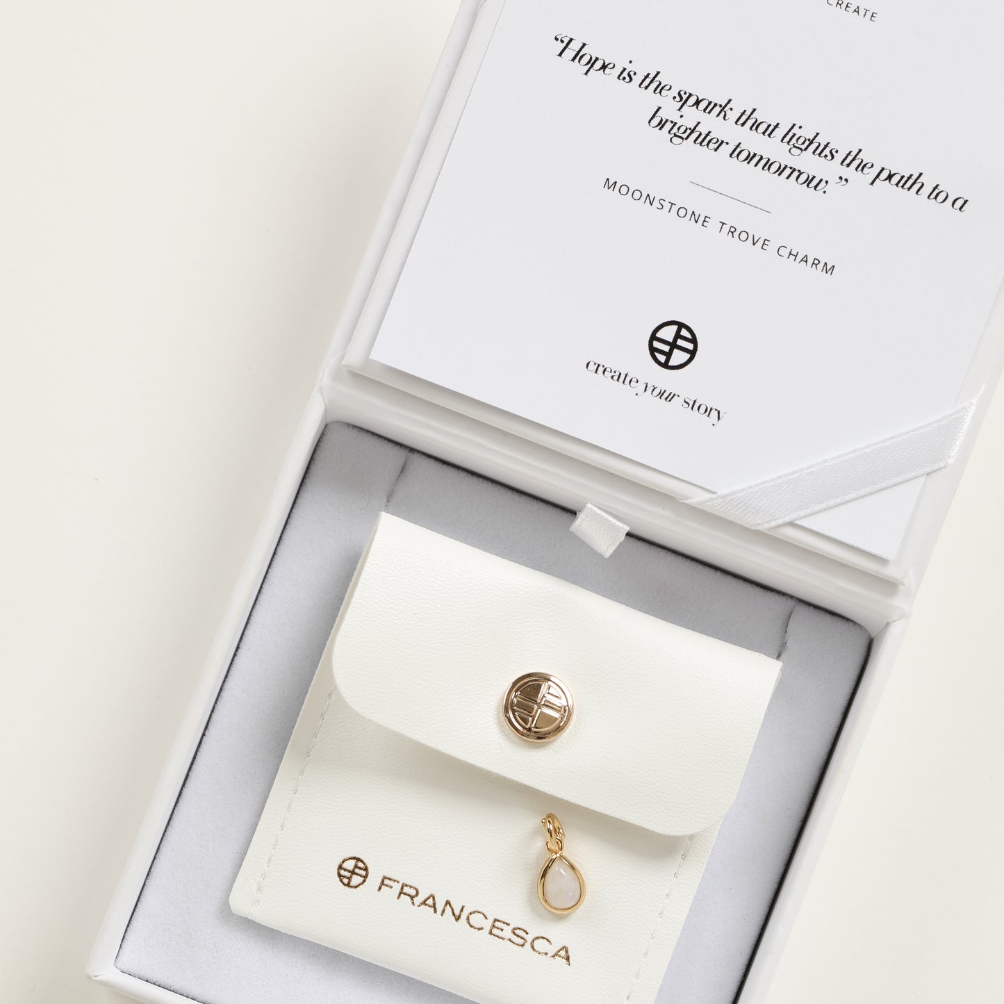 A gold charm with a teardrop-shaped moonstone in white box