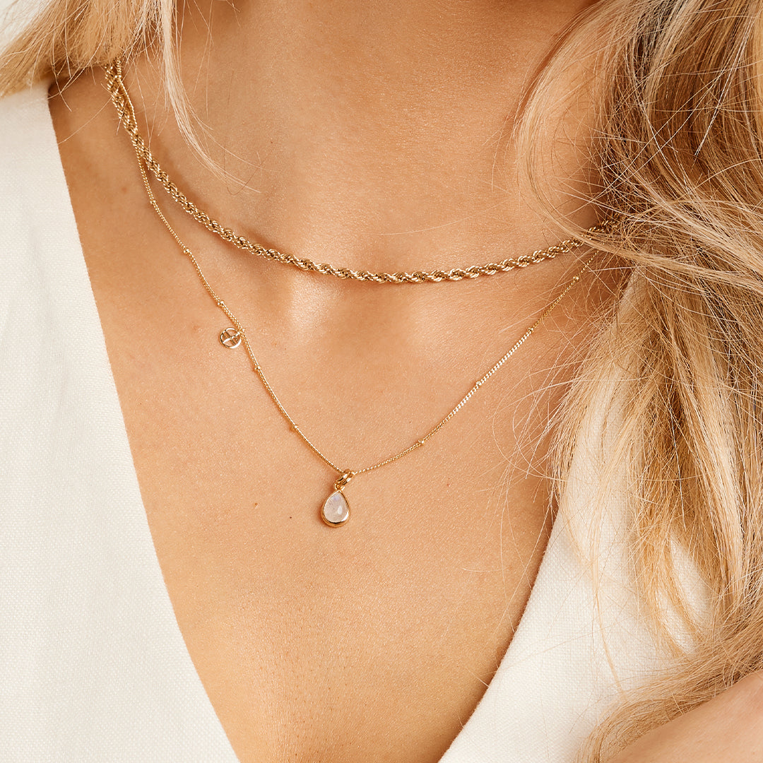 A gold charm with a teardrop-shaped moonstone on chain around neck