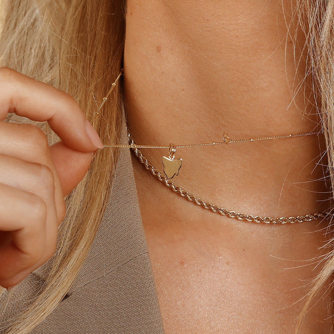 A gold-colored charm in the shape Tasmania, on a gold chain, on models neck