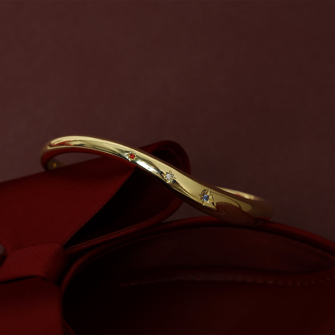 Gold cuff asymmetrical in shape with Navy, white and red cubic zirconias in a row on red background