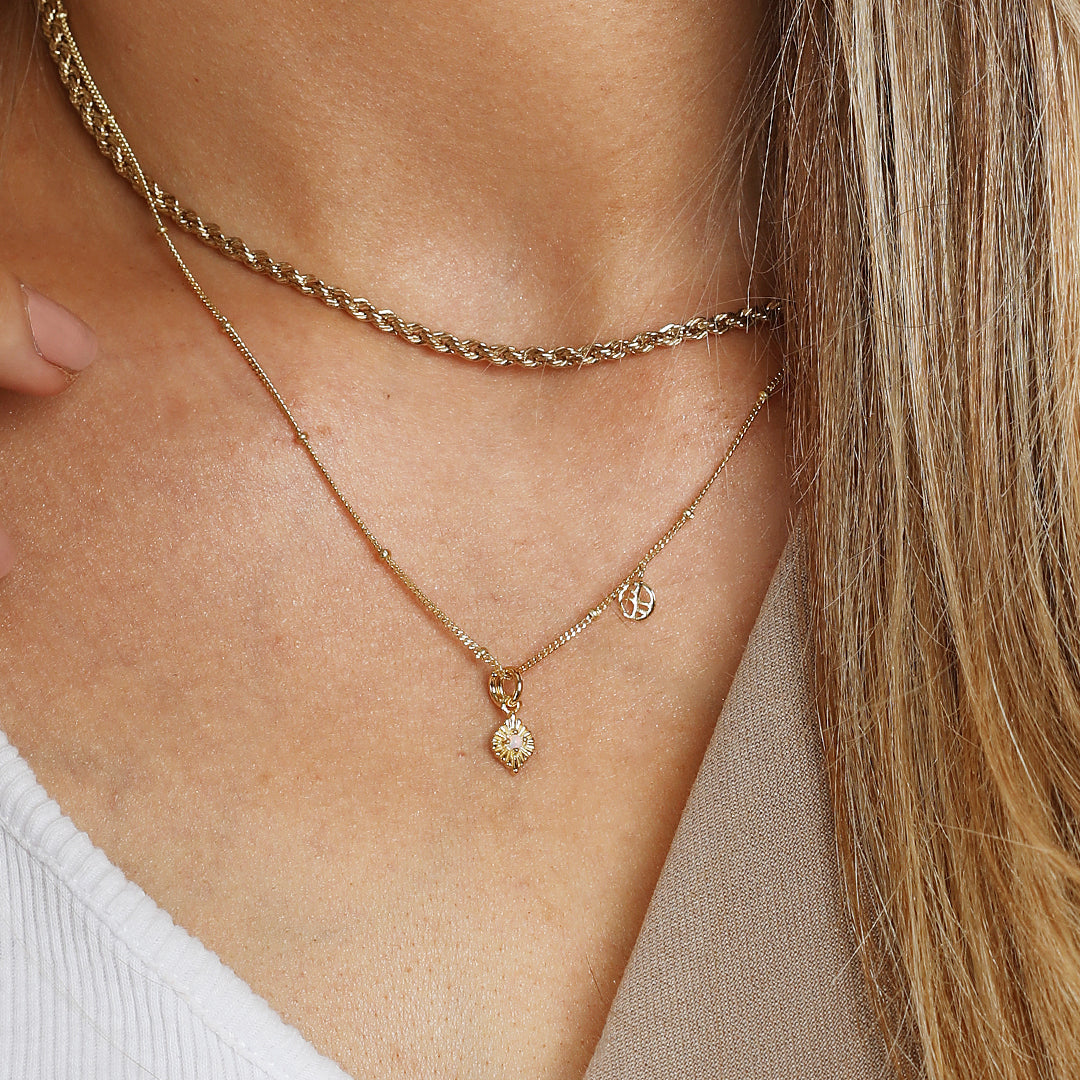 A gold diamond shaped charm with a faux opal in the centre, attached to a gold chain, worn on neck