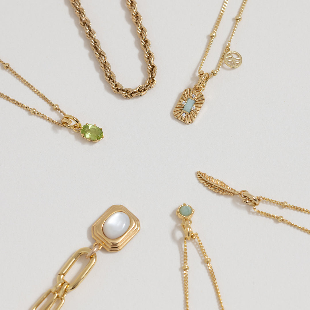 A green, oval-shaped charm pendant necklace with a silver metal chain, next to other charm necklaces