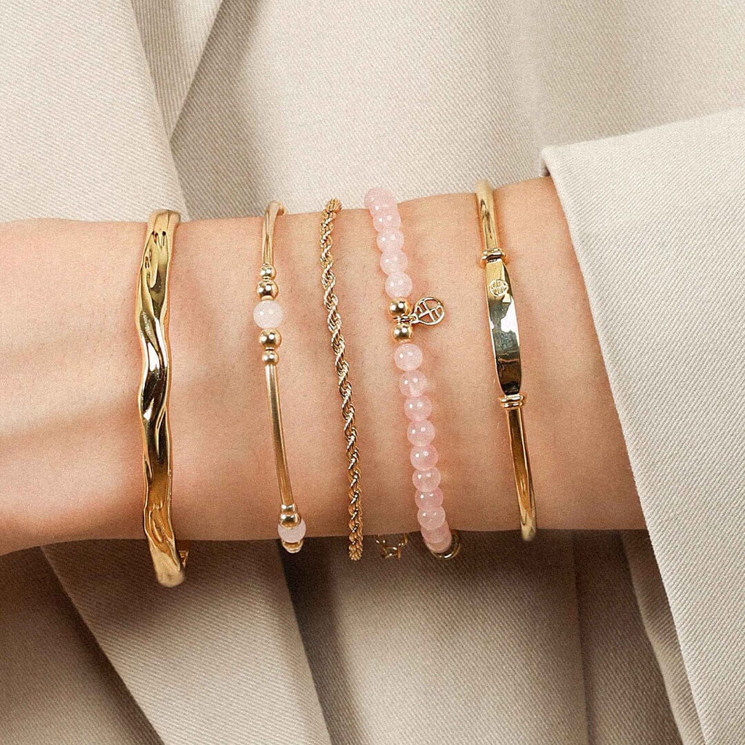 A rose quartz beaded bracelet with a gold charm, worn on the wrist with multiple bracelets