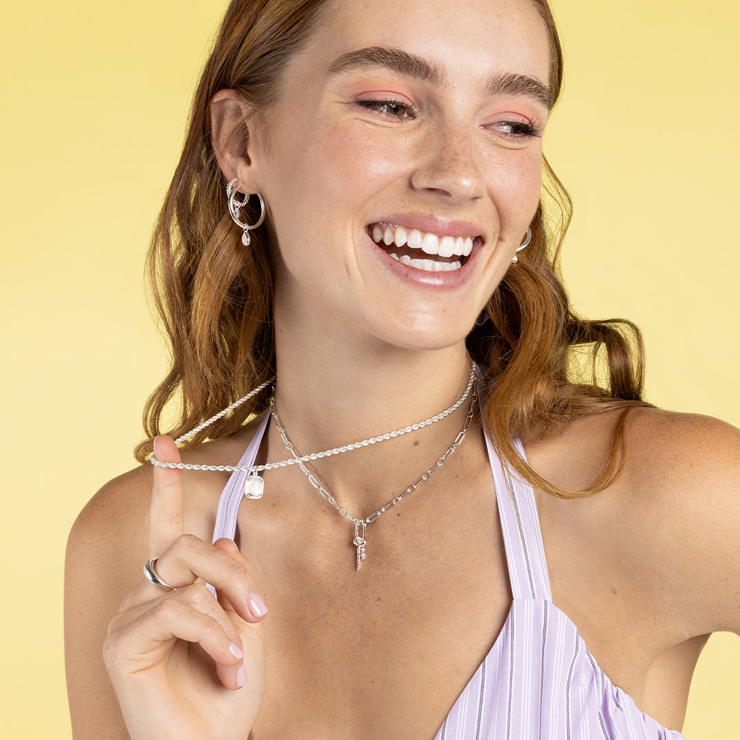 A silver-colored pendant with an oval mother-of-pearl stone in the center, on link chain, worn on models neck