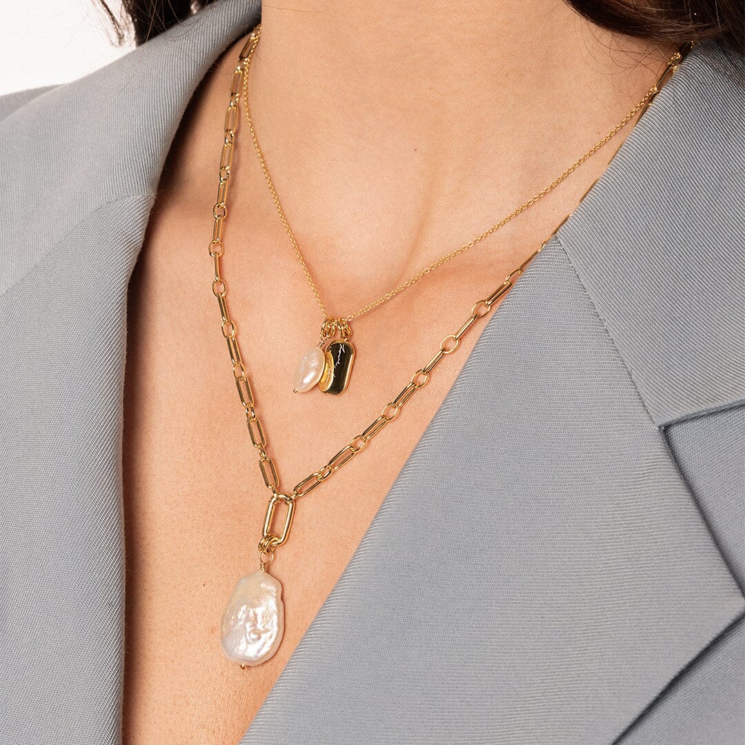 A single river pearl charm with gold findings, on gold link chain, on models neck
