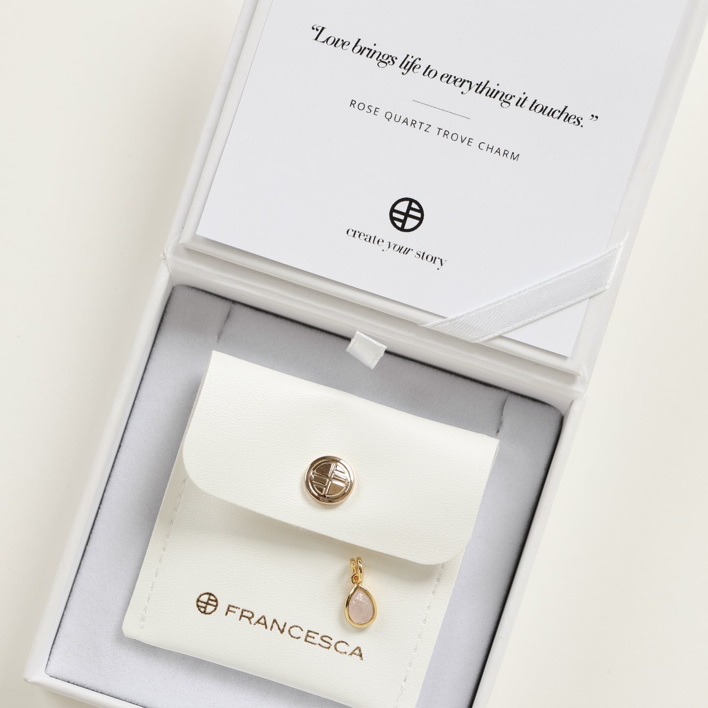 a gold charm with a tear-drop shaped rose quartz stone in a white box