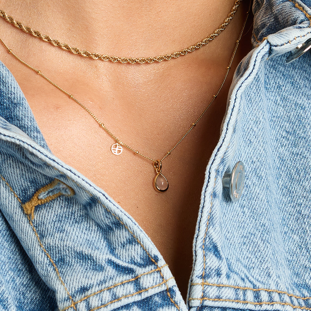 a gold charm with a tear-drop shaped rose quartz stone on a chain, around the neck