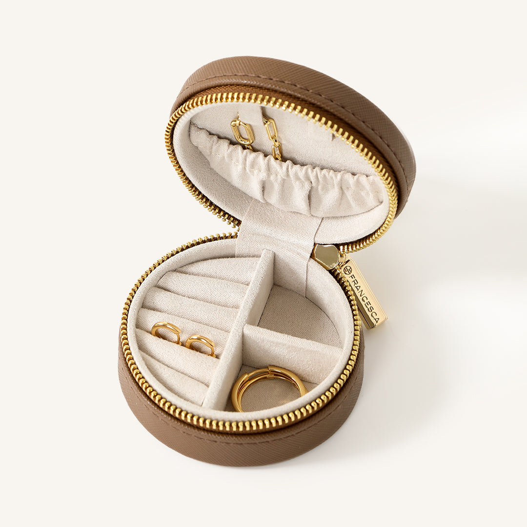 A compact round Sienna Jewellery Box made of Brown Vegan saffiano leather, opened to display its interior compartments where jewellery items like earrings are stored.