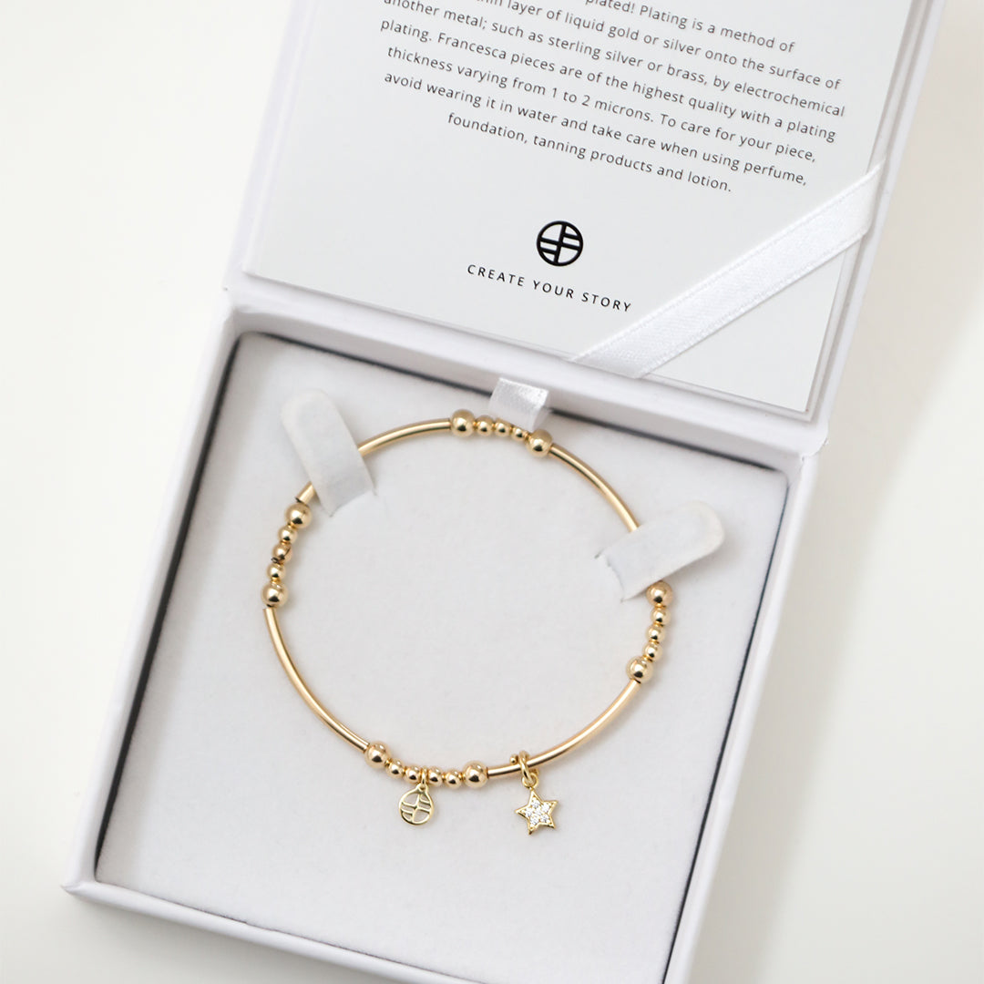 A gold-coloured bracelet with a luck star charm and small bead details displayed in white box