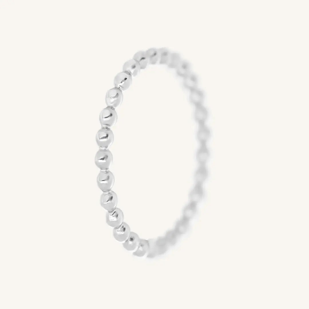 A silver coloured stacking ring with a simple, elegant design featuring small, uniform beads around its circumference.