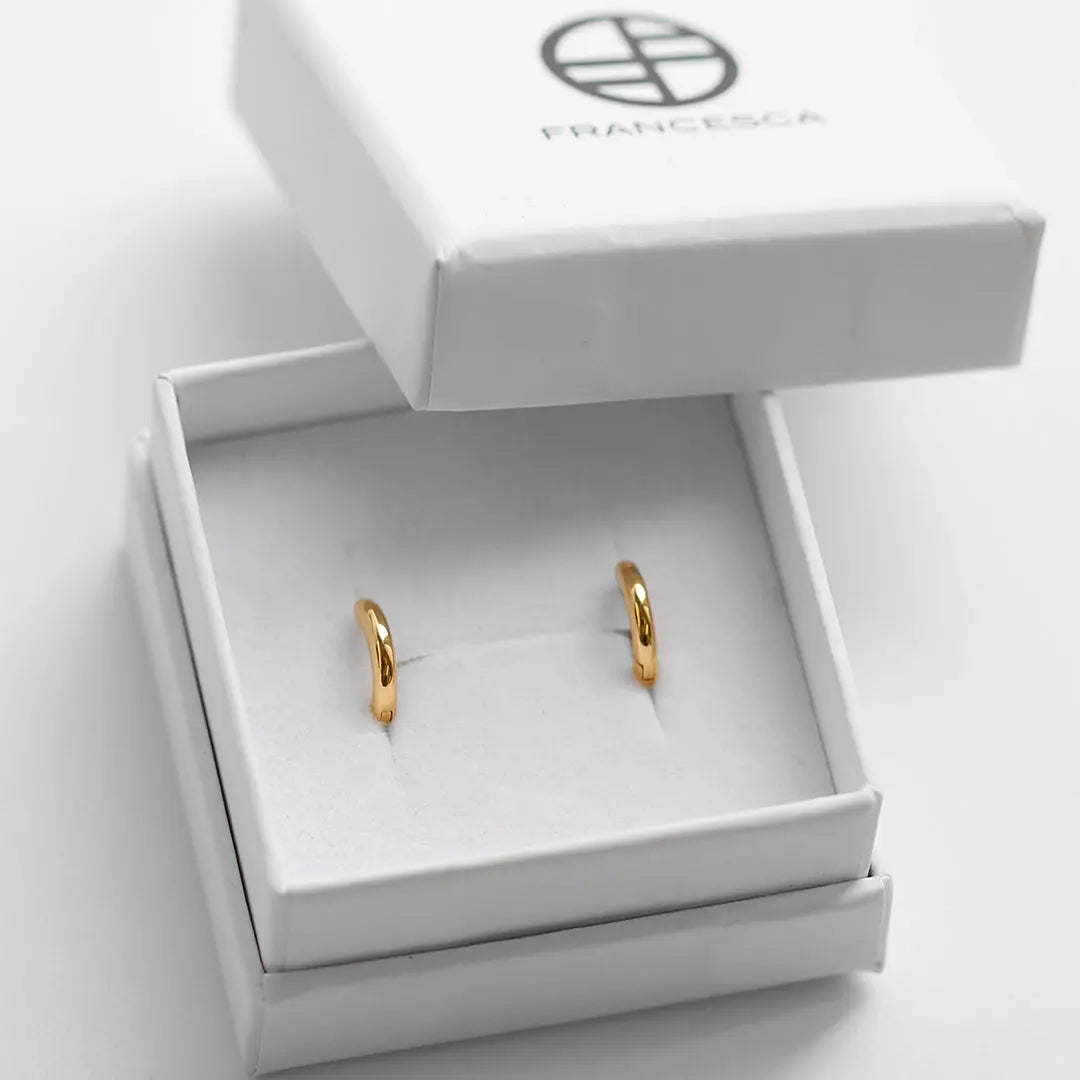 A pair of gold-colored huggie hoop earrings in a white box