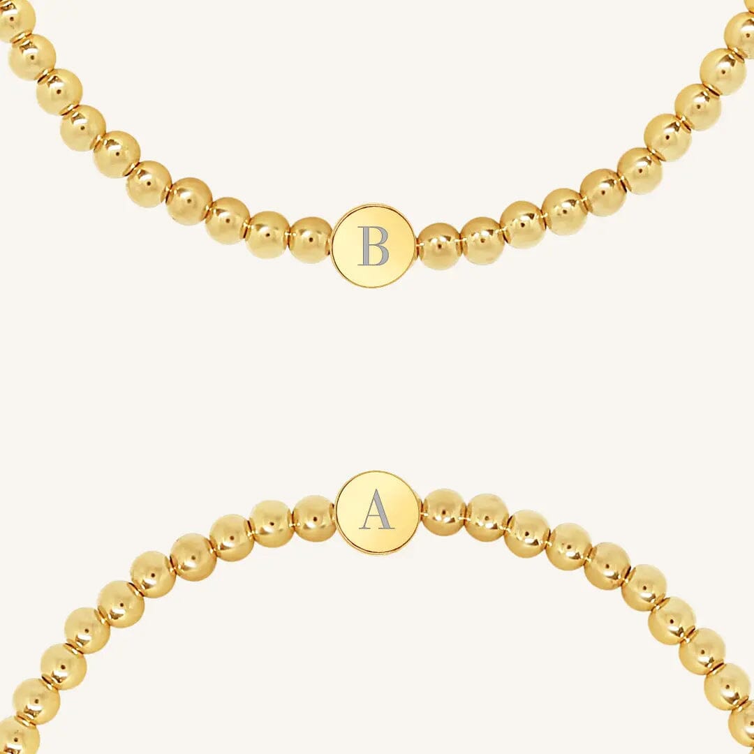 A gold bracelet with a beaded design and an engraveable bead, close up