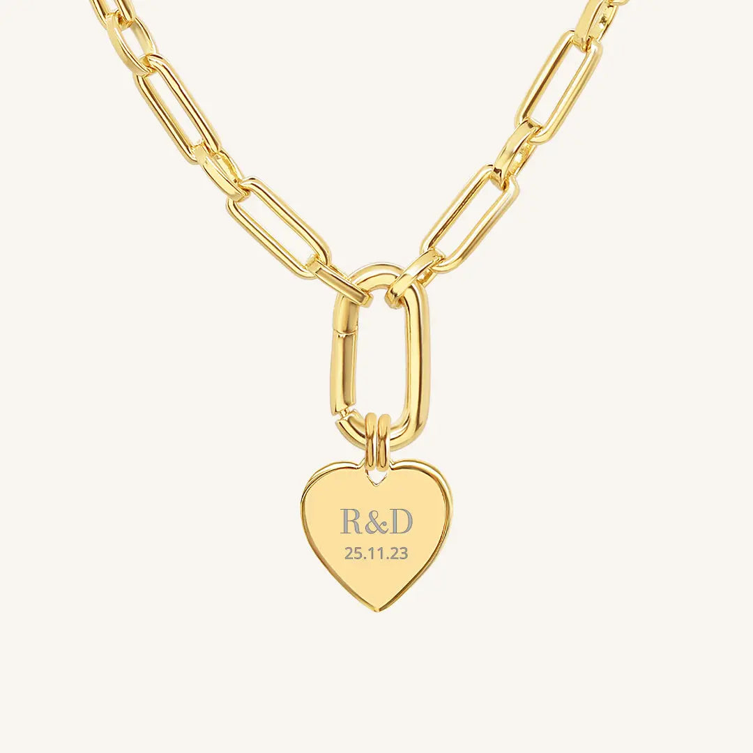 A gold heart-shaped necklace with a chain, featuring an engraved monogram initials and a date on the front.