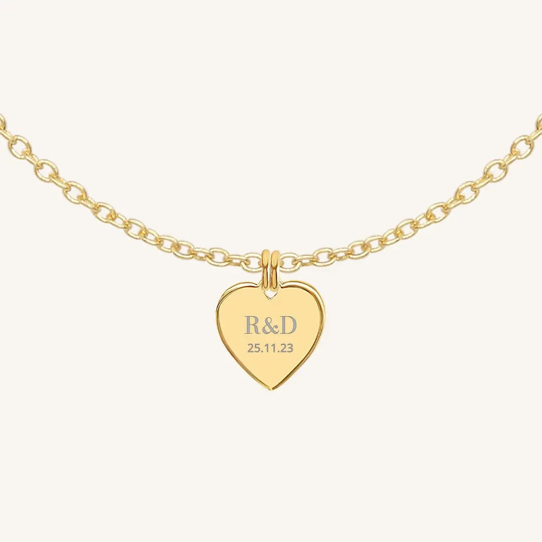 A gold heart-shaped necklace with a chain, featuring an engraved monogram initials and a date on the front.
