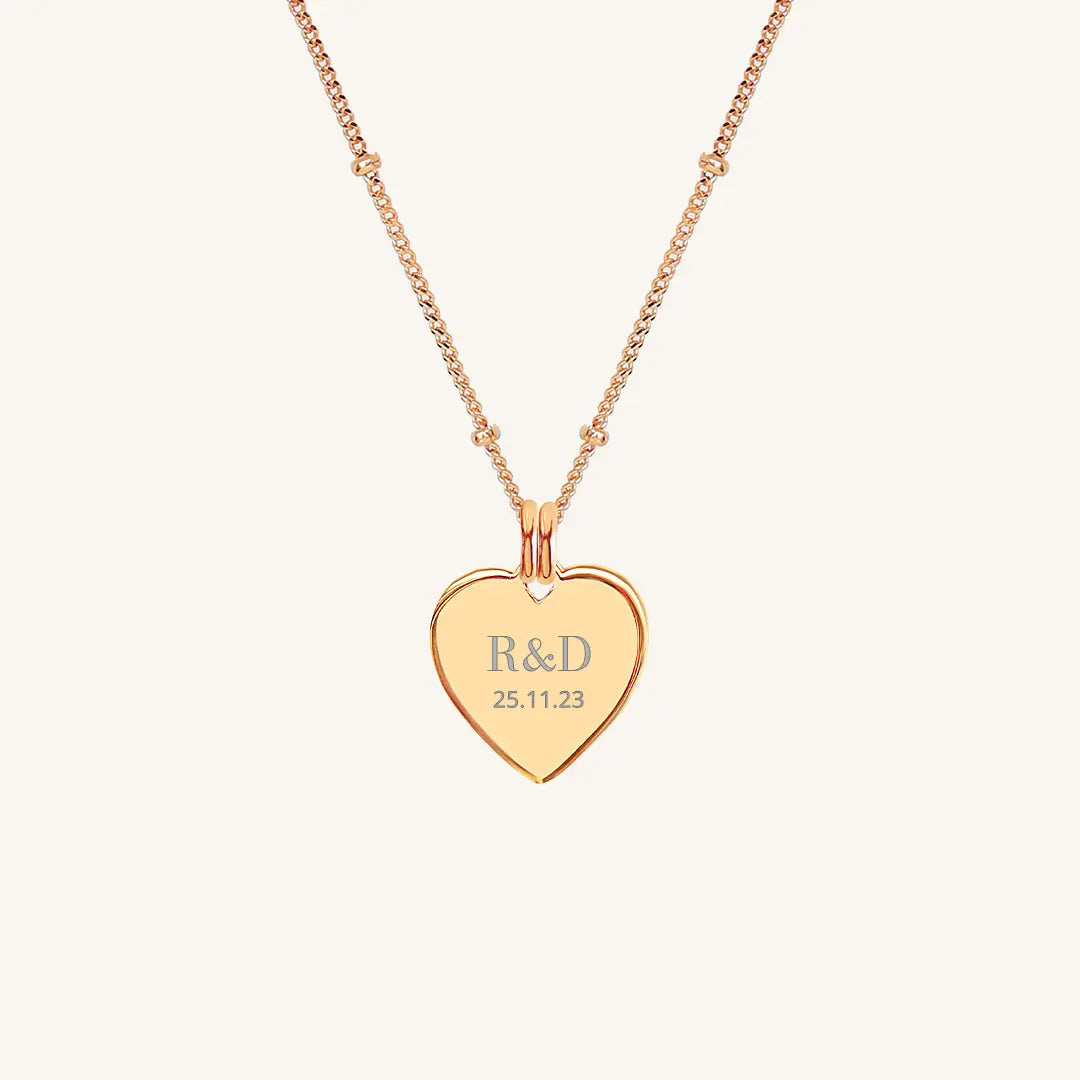 A rose heart-shaped necklace with a chain, featuring an engraved monogram initials and a date on the front.