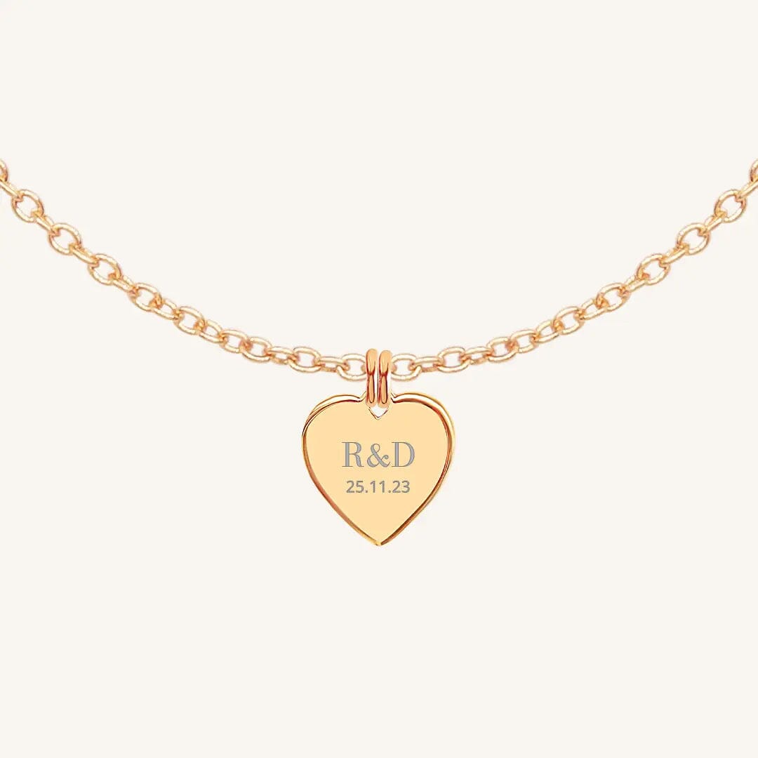 A rose heart-shaped necklace with a chain, featuring an engraved monogram initials and a date on the front.