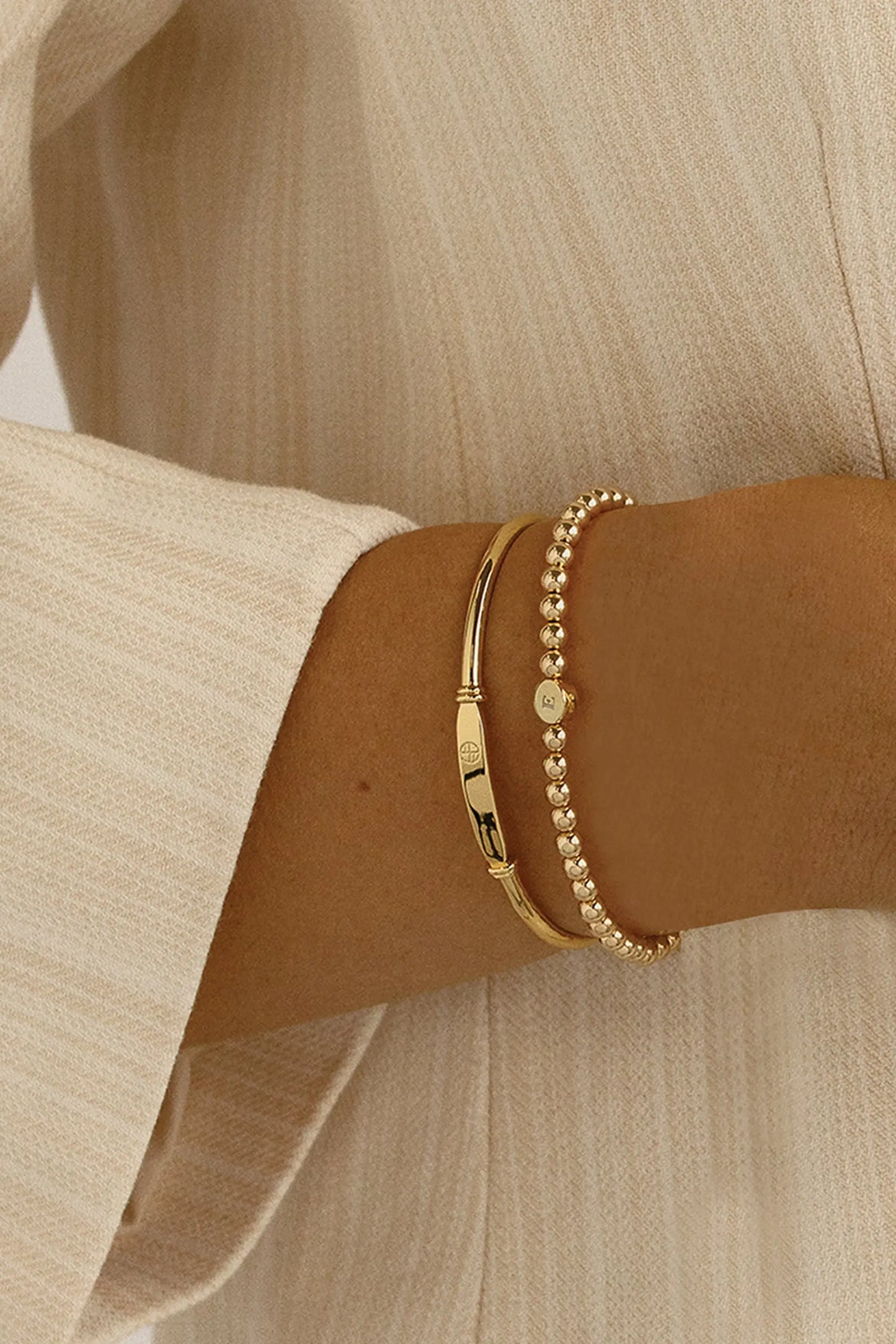A gold bracelet with a beaded design and an engraveable bead, worn on models wrist