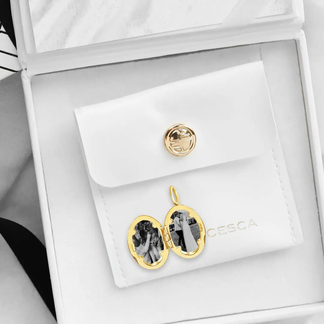 An oval-shaped photo locket with a gold metal tone, open to display two photographs, in a white box