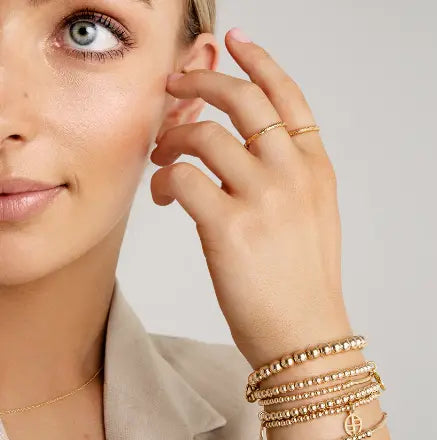 A gold-tone charm bracelet with a beaded design and a circular charm hanging from a bar, worn by model