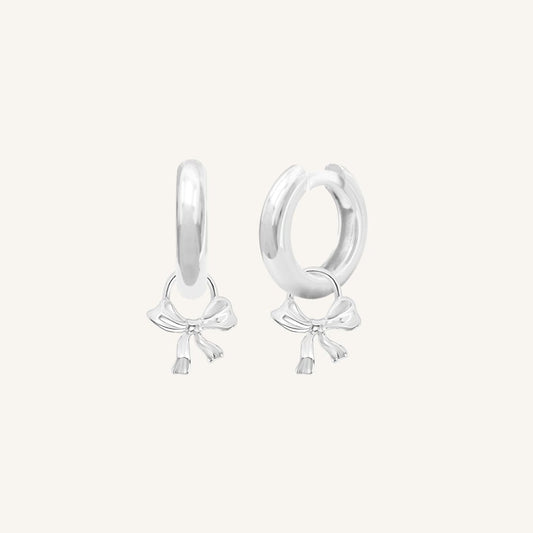 A pair of silver-coloured hoop earrings with charm pendants attached to them, displayed against a white background.