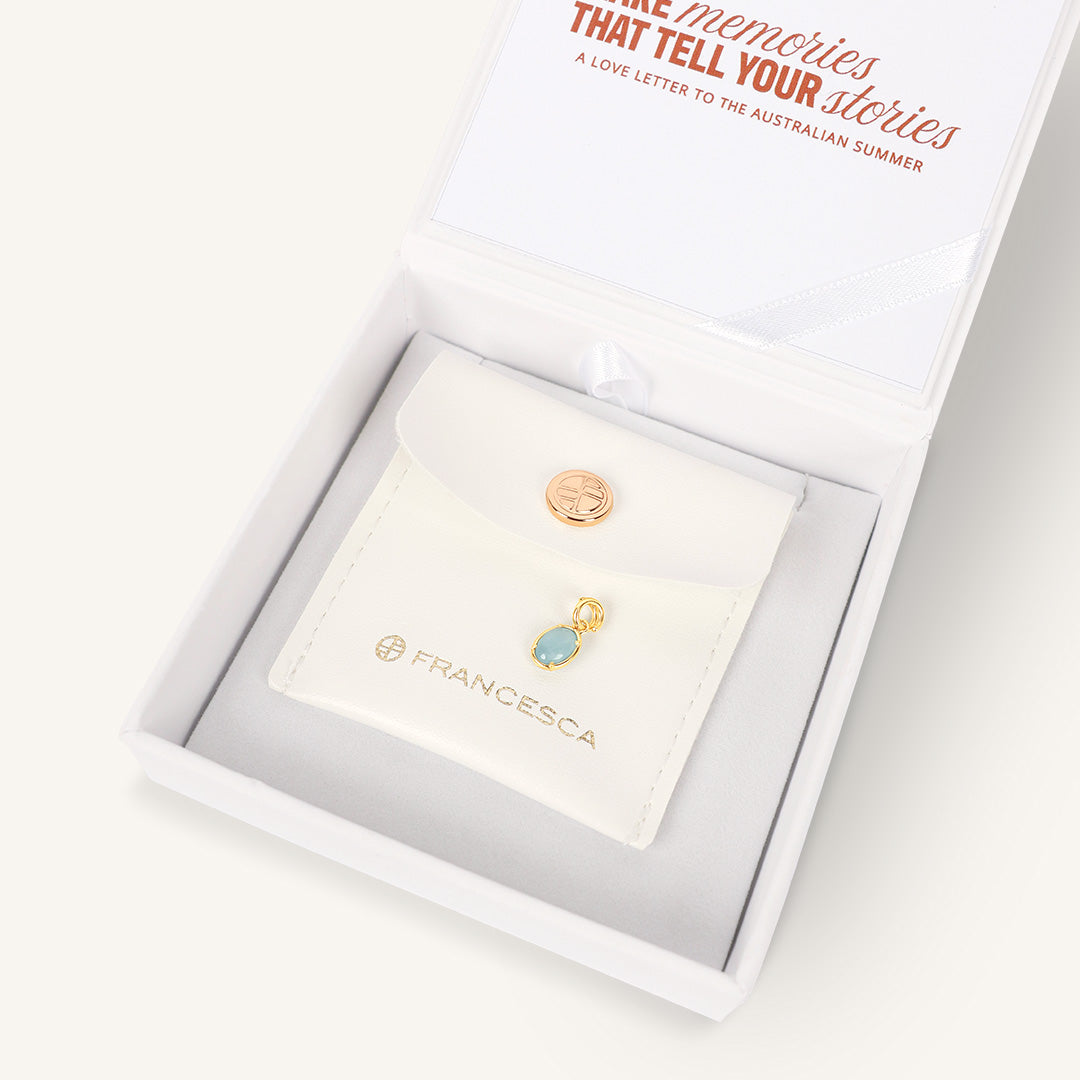 gold charm with aquamarine stone, displayed in white box 