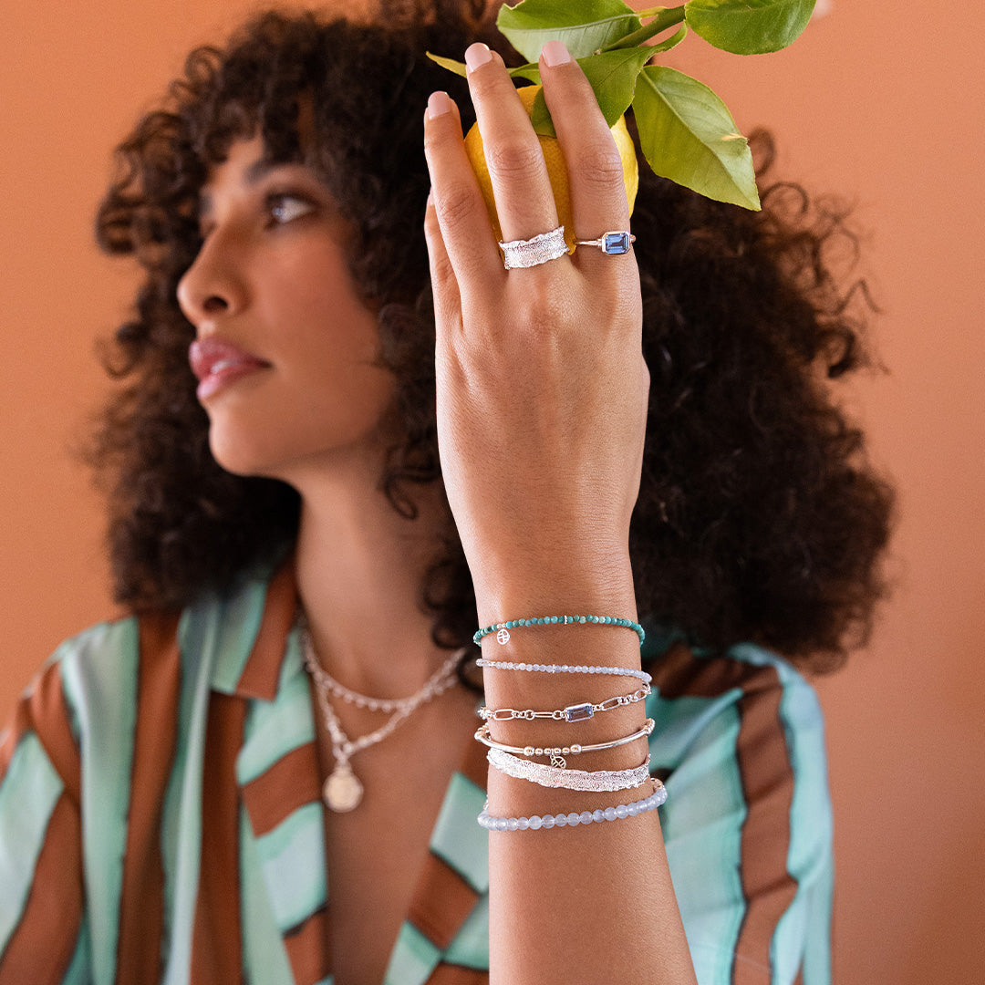 Woman wearing multiple bracelets and rings with a plant in the background
