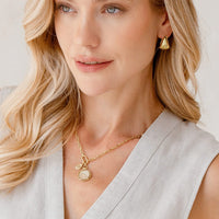 Gold pendant with a circular design and central gemstone on a light beige background