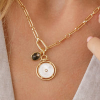 Rose gold pendant with a white circular face and central gemstone on a light beige background