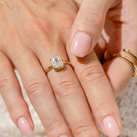 A gold-coloured ring with a white cubic zirconia, bezel set in a rectangular frame with a smooth, polished band.