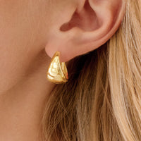 A pair of gold-colored chunky hoop earrings on a white background.
