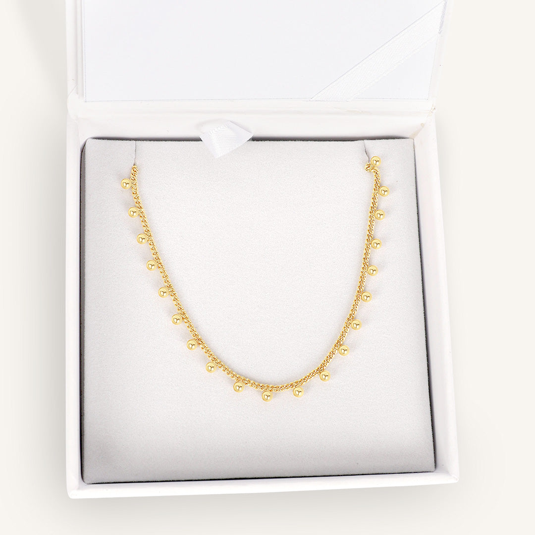 Gold necklace with small beads, displayed in white box 