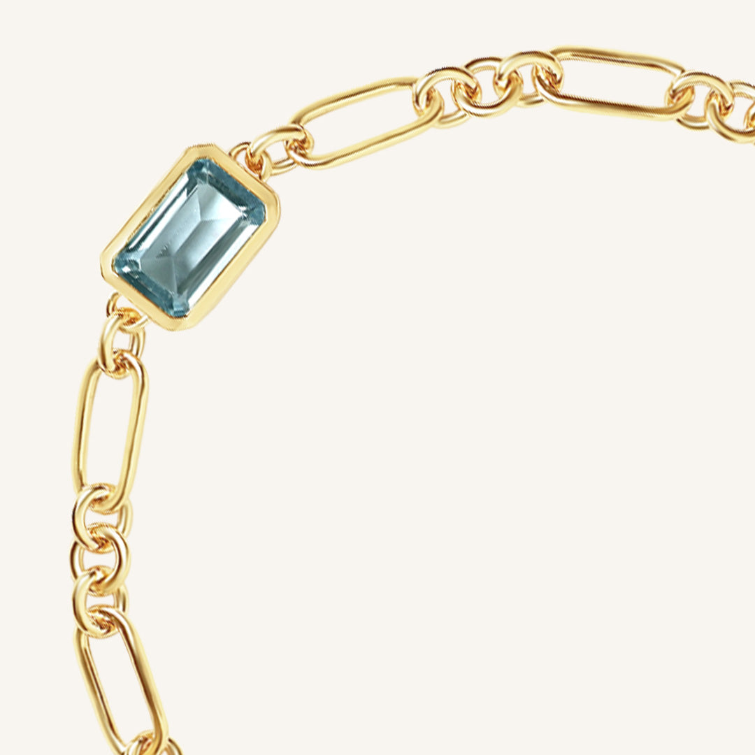 Gold chain bracelet with a blue gemstone on a white background