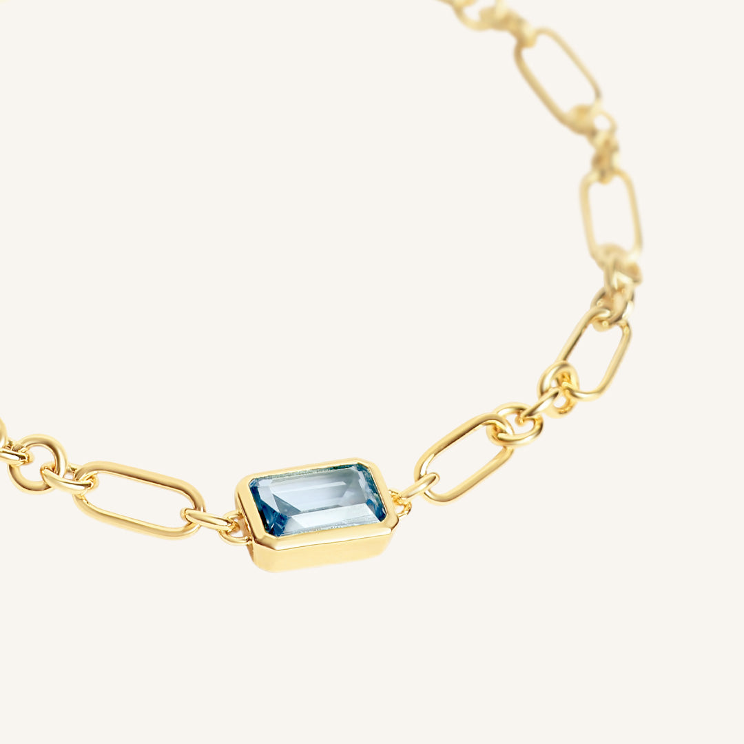 Gold bracelet with a blue gemstone on a white background