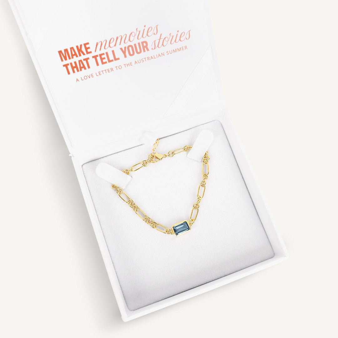 Gold bracelet with a blue gemstone, in a white box 