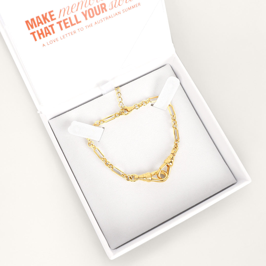 Gold chain bracelet in a white box with a card on a light gray background