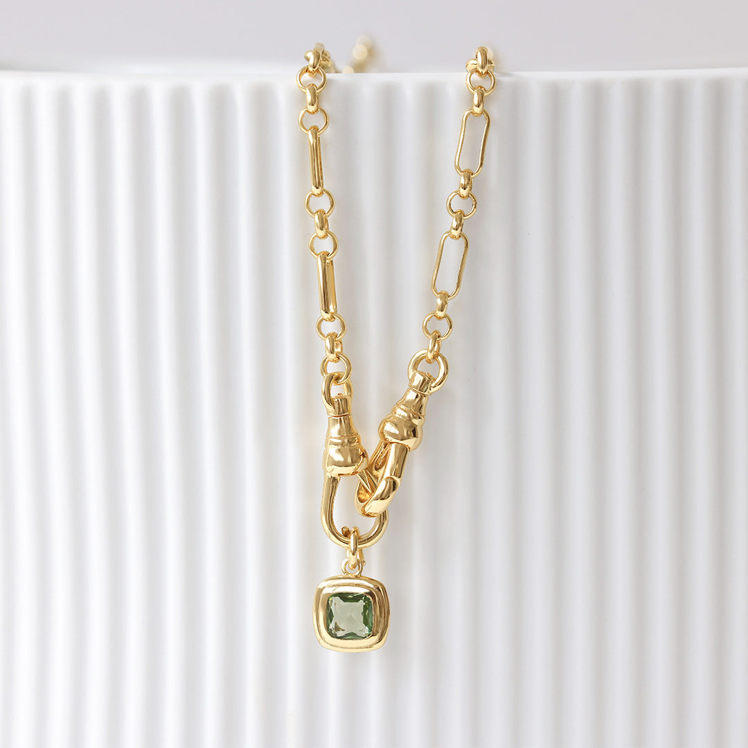 Gold necklace with a green gemstone pendant on a white background