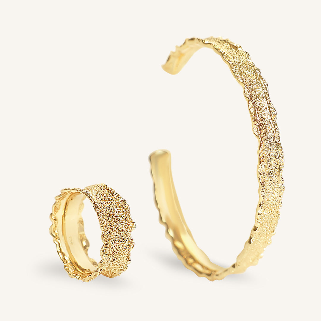 Gold ring and cuff with textured designs on a light gray background