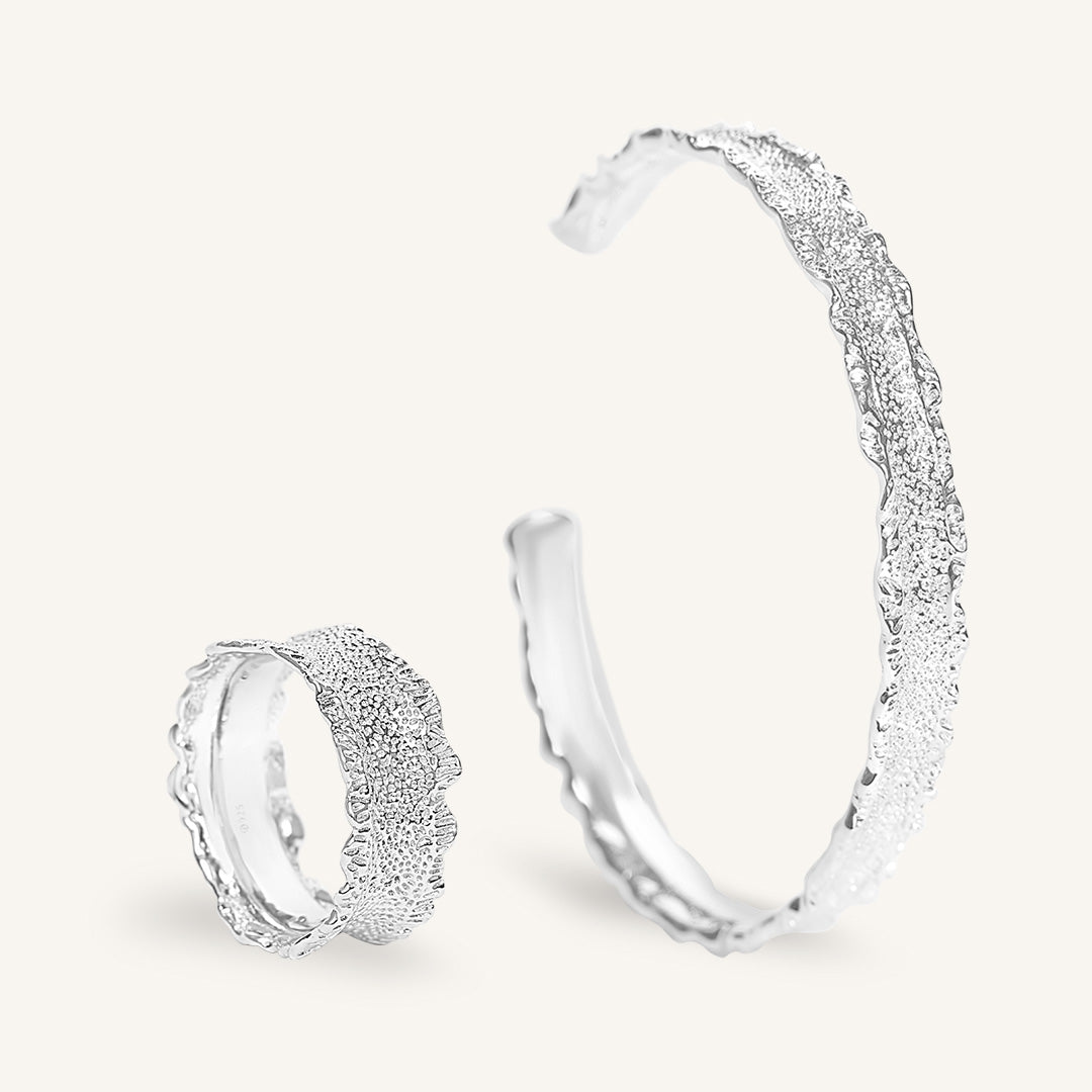 Silver ring and cuff with textured designs on a light gray background