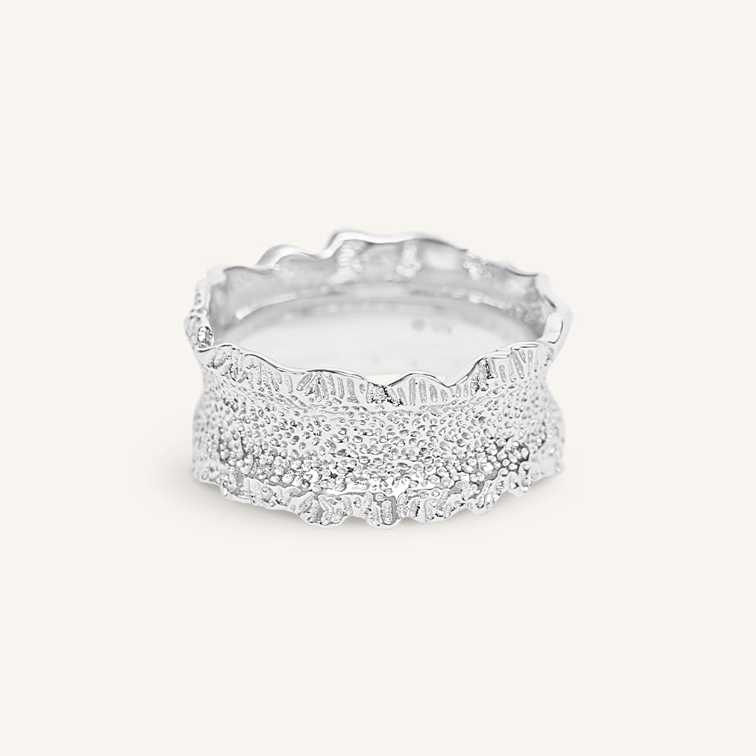 Silver ring with textured design on a white background