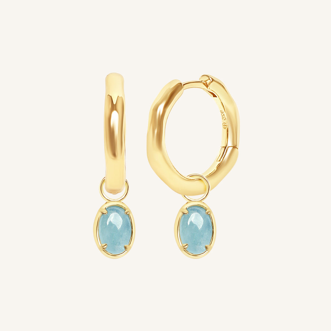 Gold hoop earrings with blue gemstones on a white background