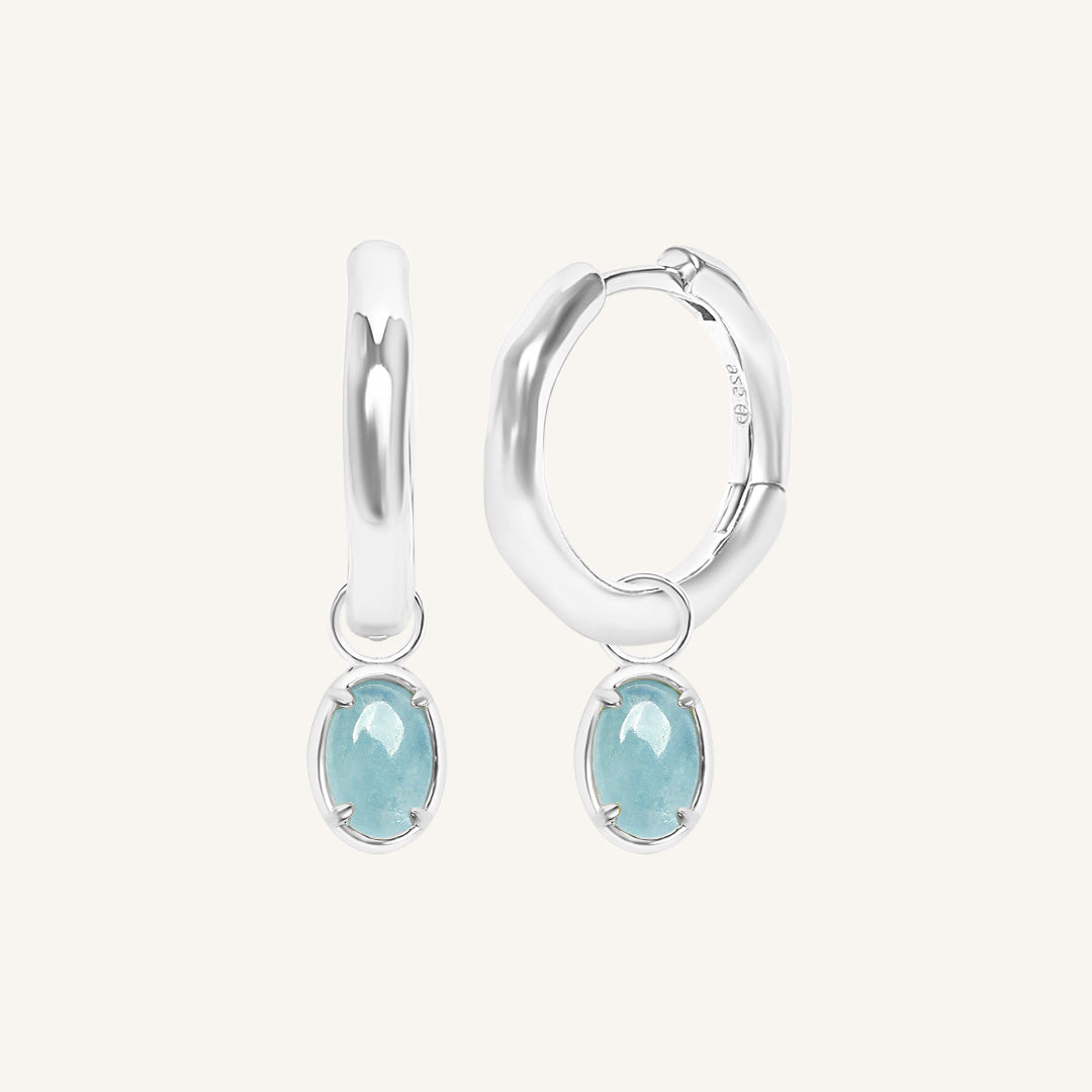 Silver hoop earrings with light blue gemstones on a white background