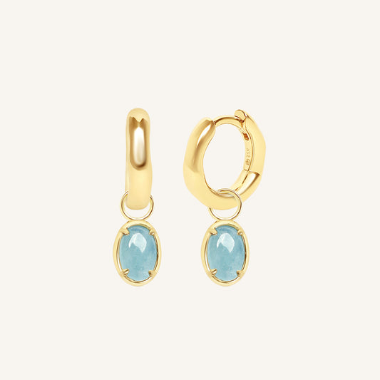 Gold hoop earrings with blue gemstones on a white background