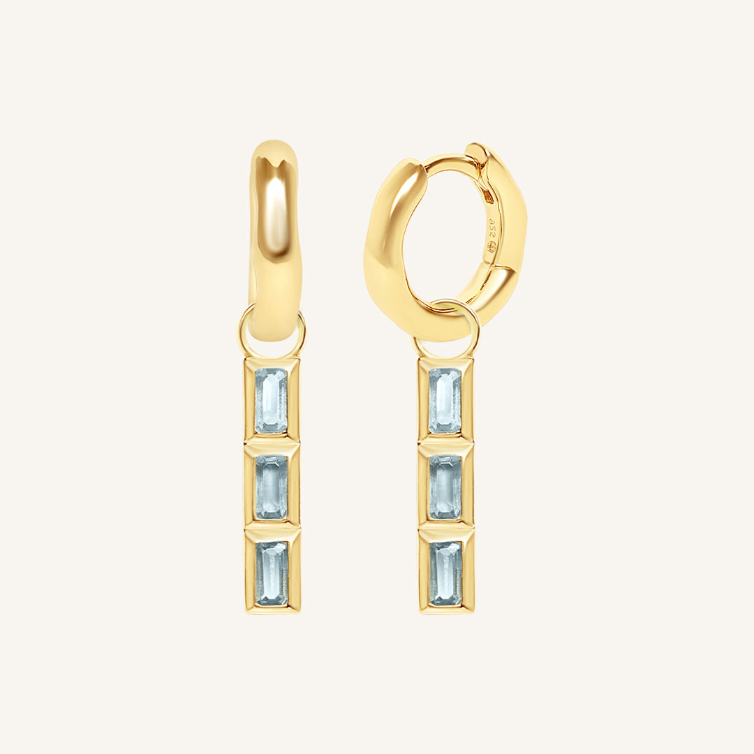 Gold hoop earrings with blue gemstones on a white background