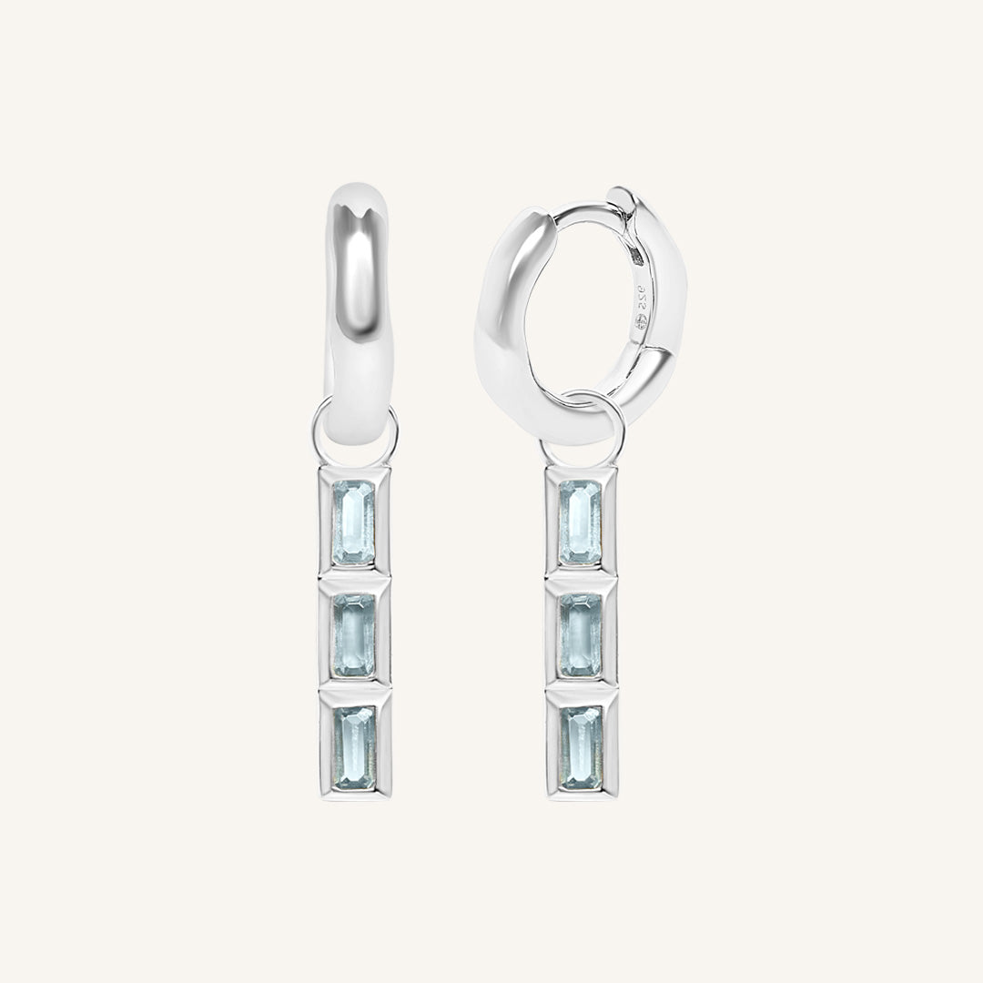 Pair of silver hoop earrings with blue gemstones on a white background