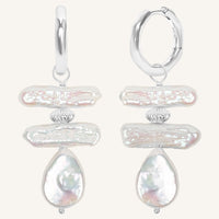 Pair of silver hoop earrings with teardrop-shaped pearls on a white background