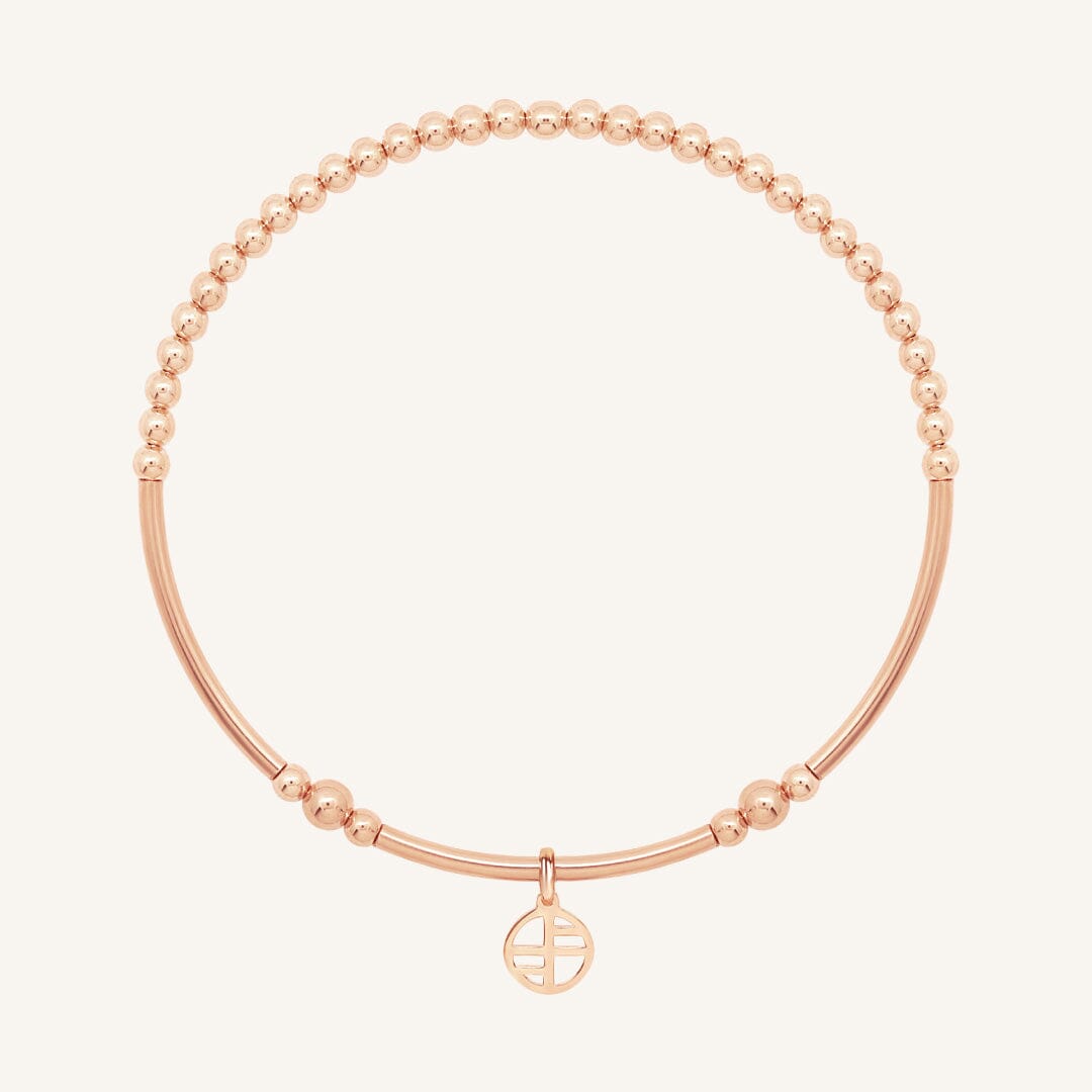 Rose gold bracelet with a small charm on a white background