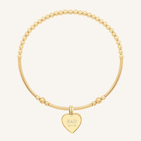 A gold bracelet with a beaded design and a heart-shaped charm, engraved with initials and a date 