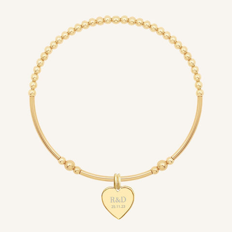 A gold bracelet with a beaded design and a heart-shaped charm, engraved with initials and a date 
