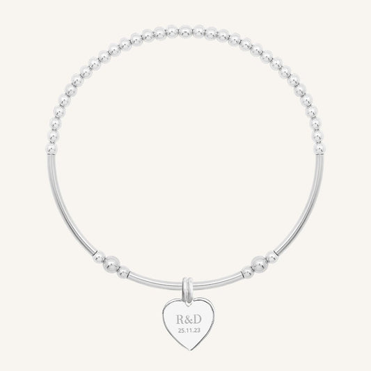 A silver bracelet with a beaded design and a heart-shaped charm, engraved with initials and a date 