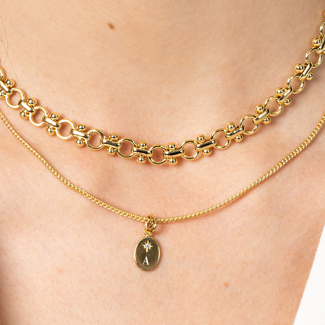 Two gold necklaces on a person's neck with one featuring an 'A' pendant.